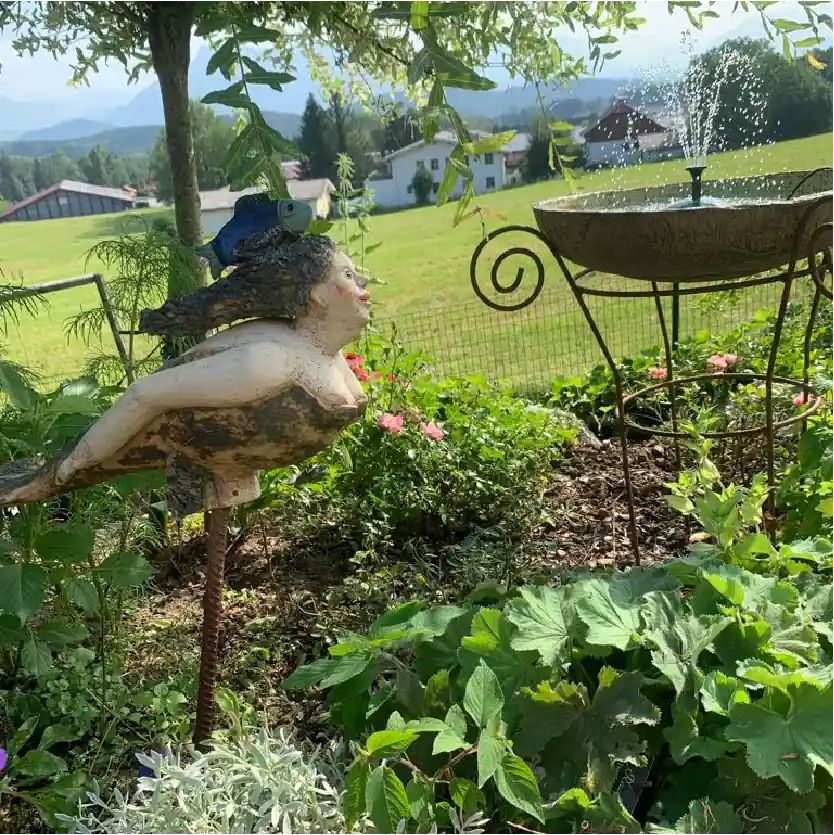 Ein kleiner Springbrunnen aus Keramik und eine Badenixe aus Keramik vor einer Grünen Wiese an einem Somertag.