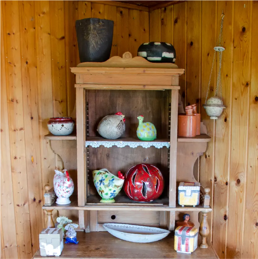 Eine Vielzahl an Hühner, Kugeln, Flaschen, Vasen und Schatullen aus Keramik in einem alten Bauernschrank aus Holz.